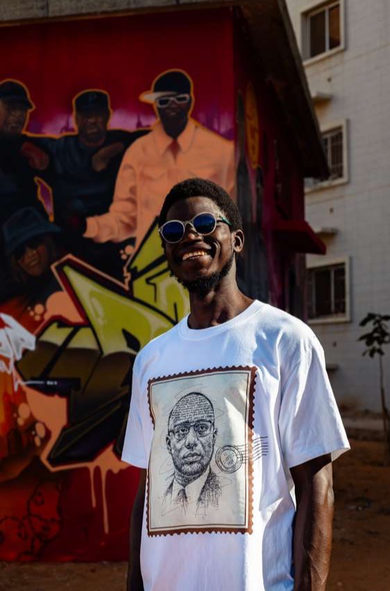 Modèle en t-shirt blanc Asrafobawu (collection INDIGO) devant une fresque murale
